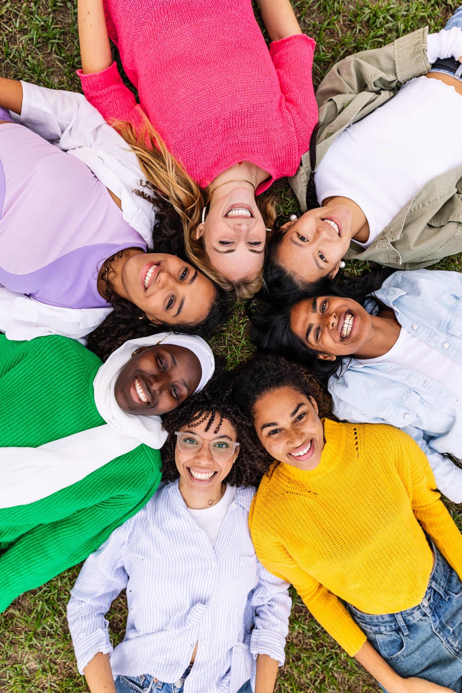 High angle view. Portrait of diverse happy women looking at camera lying together on grass at city park. Happiness, female friendship and youth community concept.